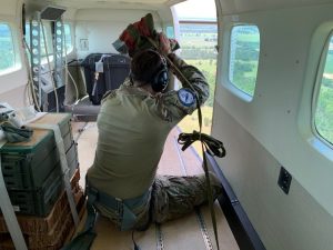 A view from within the aircraft shows an instructor preparing to toss the SATB while the aircraft is aloft.